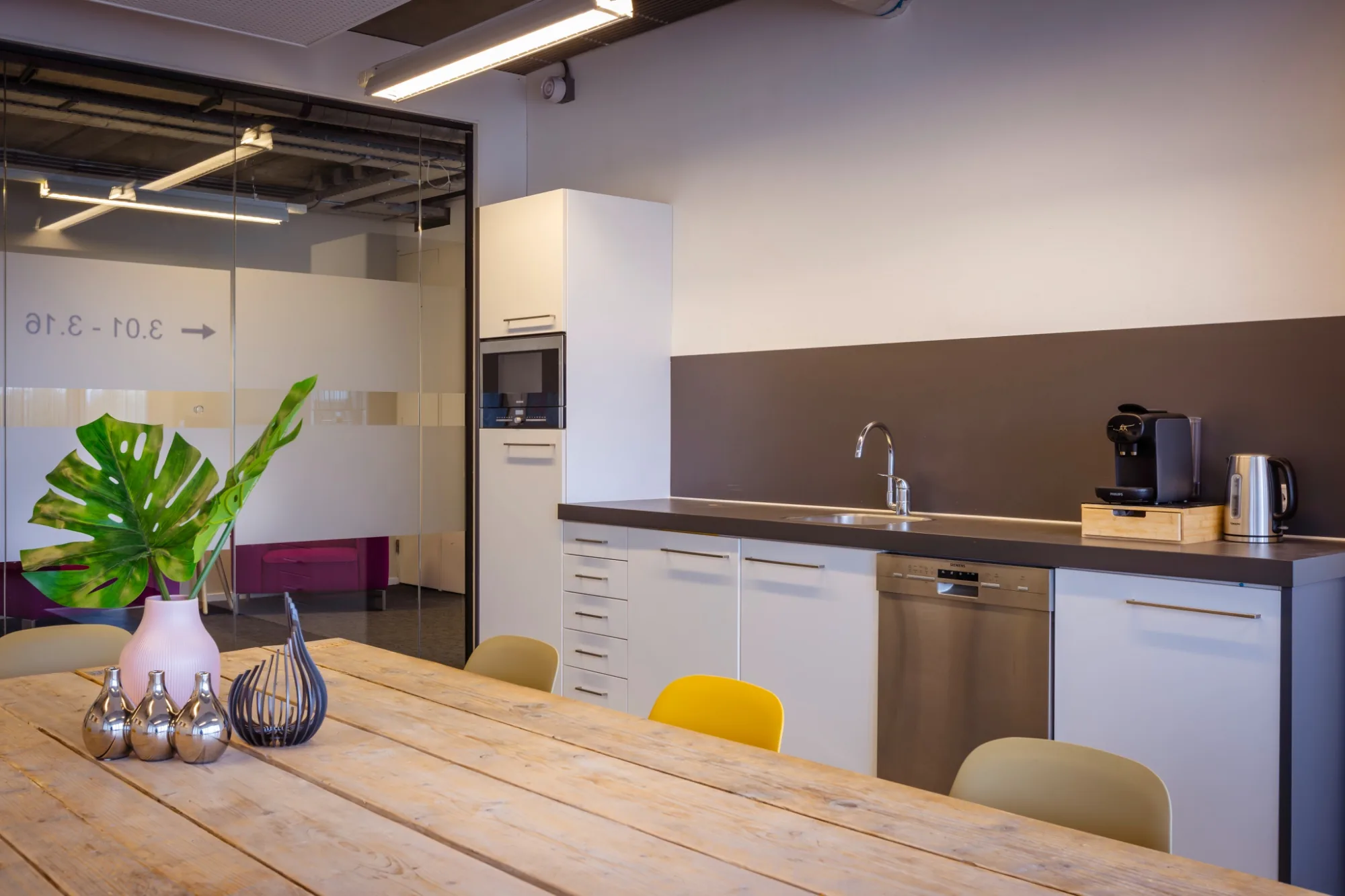 Pantry met witte keukenkastjes, koffiemachine en houten eettafel met gele en groene stoelen