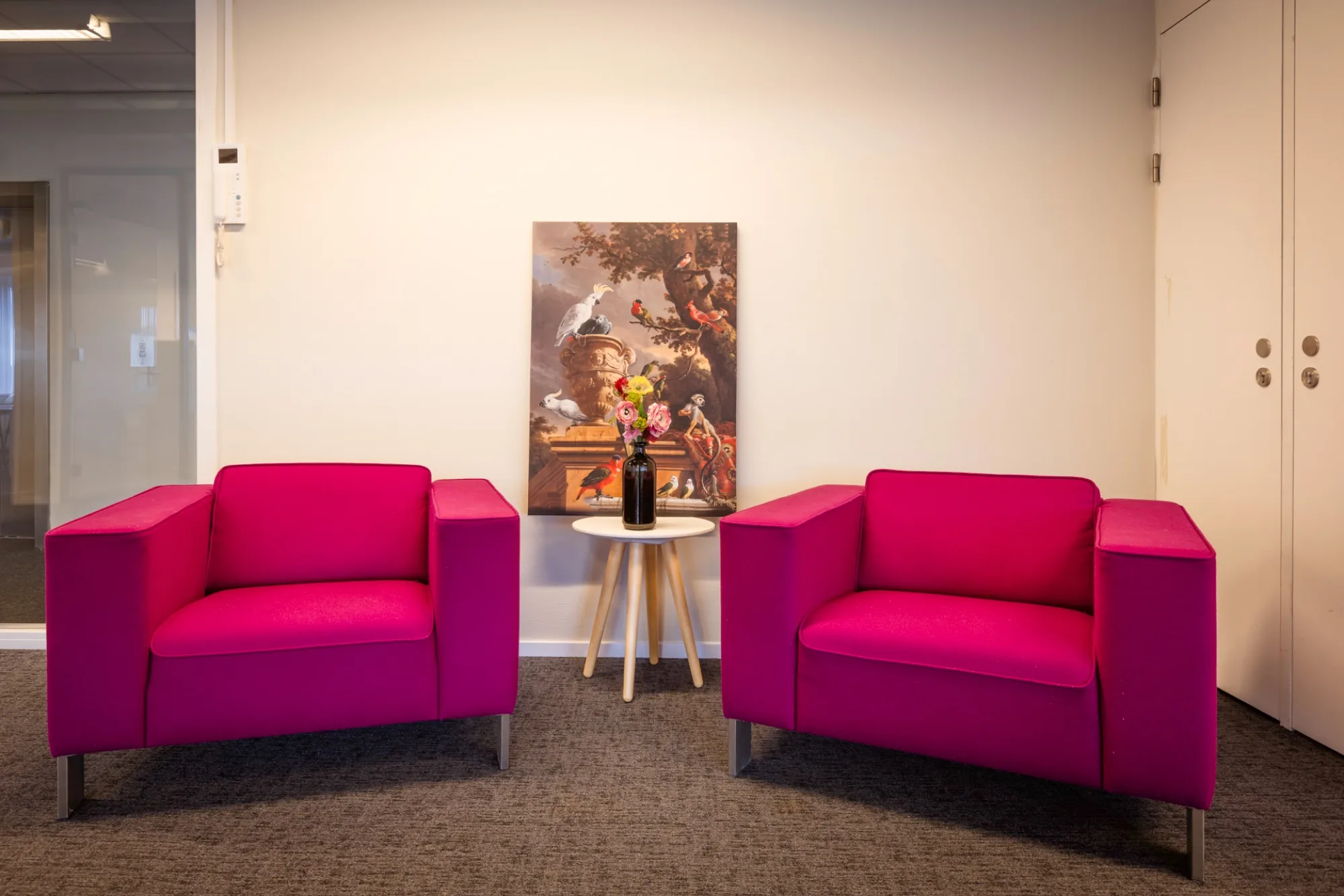 Wachtruimte met twee fuchsia fauteuils, ronde bijzettafel en klassiek vogelsschilderij als wanddecoratie