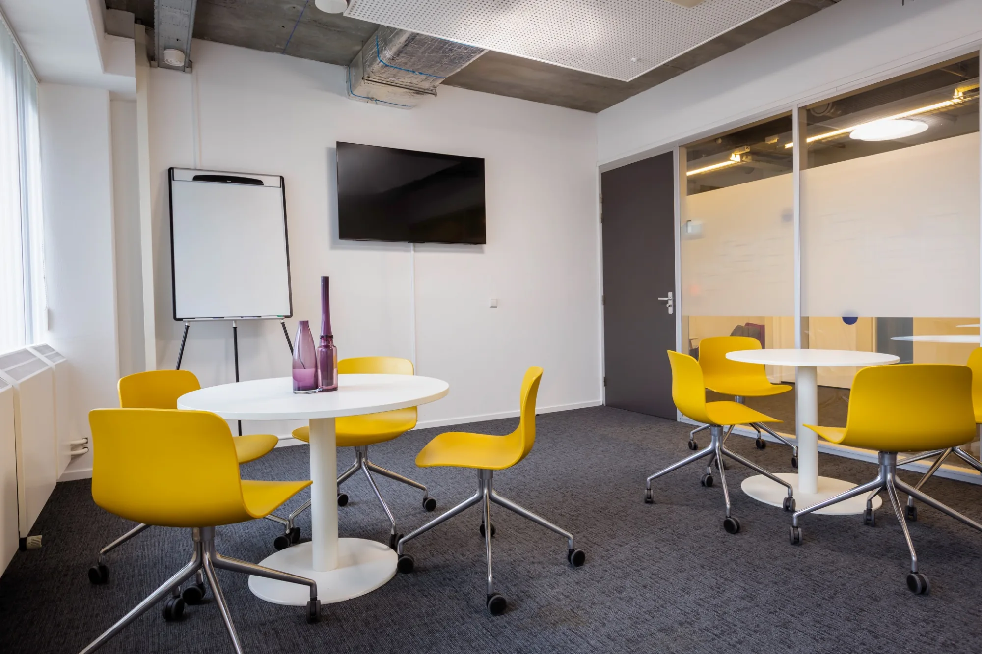 Gang met rode loungezitplaats, bloemenschilderij, hangplanten en glazen kantoorwanden met grafische raamfolie