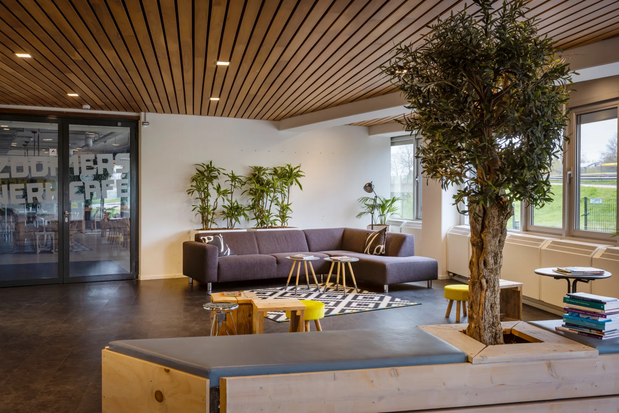 Flexibele overlegruimte met ronde witte tafels, gele wielstoelen, flatscreen en whiteboard